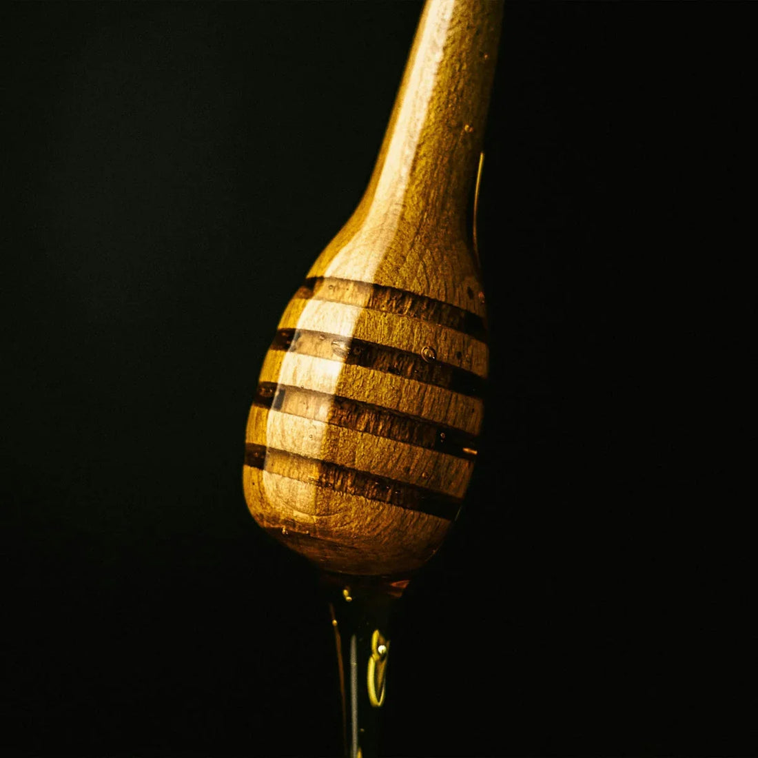 Close-up of wooden honey dipper with golden honey dripping against black background