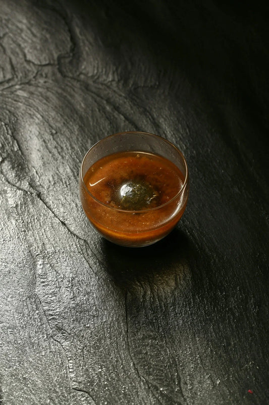 Glass cup with brown liquid and a dark ball in the center on textured black surface
