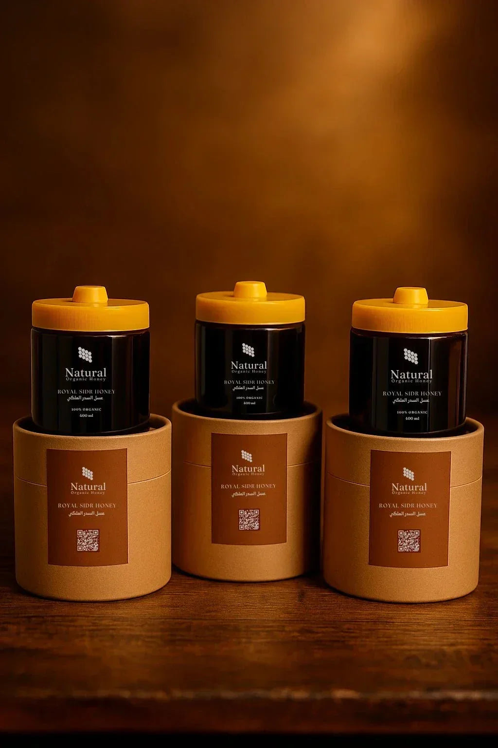 Three jars of Natural Organic Royal Sidr Honey with yellow lids on round brown packaging on wooden surface